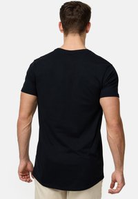 Camiseta de algodón negra con cuello redondo y mangas cortas, que presenta un dobladillo recto y una textura suave. La vista posterior muestra un diseño minimalista.