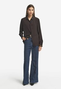Schwarzes Langarmshirt mit Knopfleiste, kombiniert mit weitem blauen Denim-Jeans. Der Stoff wirkt glatt und hat eine lässige Passform.