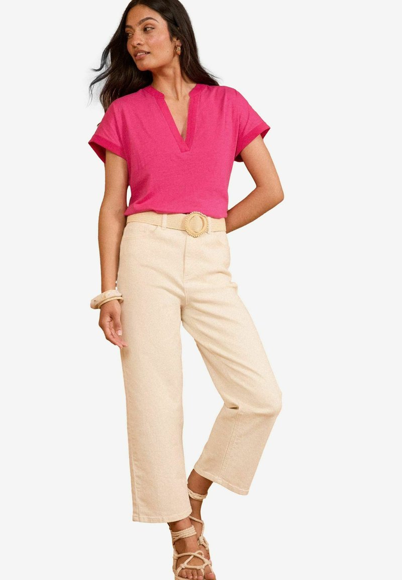 Top rosa de manga corta con escote en V, combinado con pantalones de pierna ancha color crema sujetos con un cinturón tejido circular, y sandalias planas.