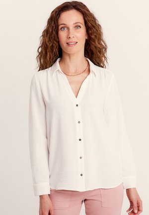 Witte langslijfshirt met een knoopsluiting aan de voorkant, een v-halskraag en contrasterende zwarte knopen. De stof lijkt lichtgewicht en structuur te hebben.