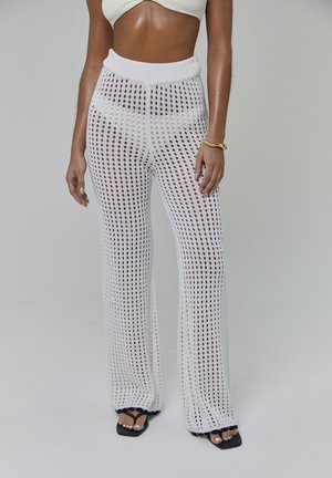 Pantalones de crochet blancos de punto con una pretina alta, que presentan un diseño de tejido abierto y transparente y corte de pierna acampanada.