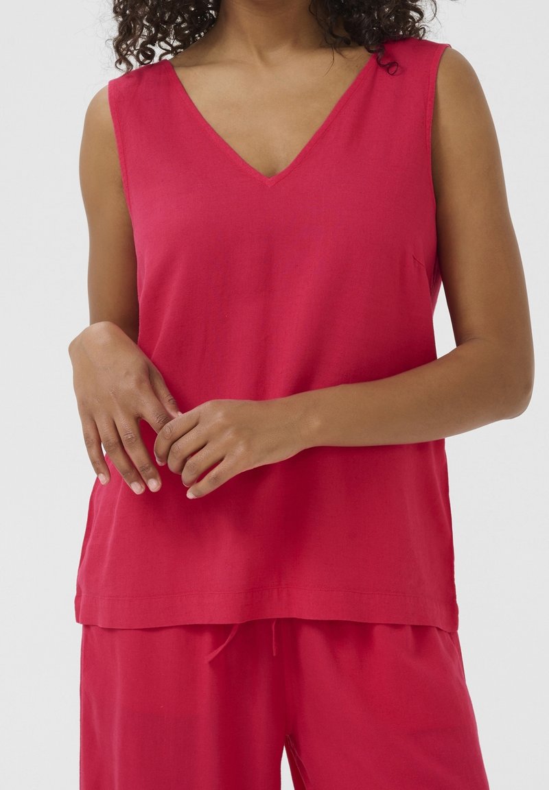 Haut sans manches fuchsia avec un col en V, fabriqué dans un tissu lisse et léger. Présente une coupe décontractée et un ourlet uniforme.