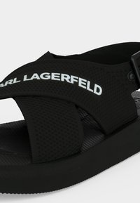 Μαύρο σανδάλι με υφή, ρυθμιζόμενα λουράκια και λευκό λογότυπο "KARL LAGERFELD" στο πάνω λουράκι.