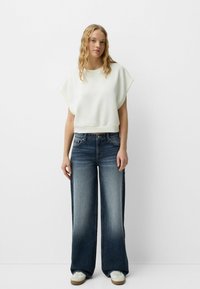 Ljust grå oversized sweatshirt med korta ärmar, i kombination med vida, blekta blå jeans och vita sneakers.
