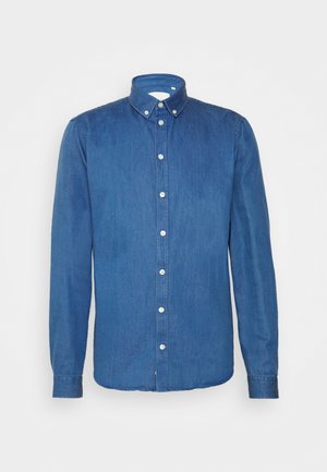 Camisa de mezclilla azul oscuro, con botones, de manga larga, cuello puntiagudo y botones blancos en la parte delantera, que presenta un dobladillo ligeramente curvado.