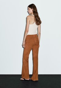 Bruna mockaskinnflared byxor med en slät textur, kombinerade med en ljusbeige linne. Modellen ses bakifrån mot en neutral bakgrund.