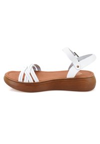 Witte strappy sandaal met een ronde neus, platte bruine rubberen zool en een verstelbare enkelband. Gladde textuur met contrasterende materialen.