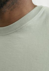 Lys grøn T-shirt med rund halsudskæring, glat tekstur og synlige sømdetaljer på kraven. Kortærmet, afslappet design.