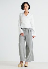 Blusa blanca de manga larga con un diseño sencillo y limpio, combinada con pantalones de pierna ancha a rayas grises y zapatos de esparto color tostado.