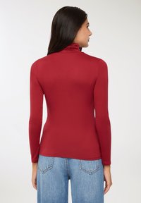 Czerwona bluzka z długim rękawem i kołnierzykiem typu mock neck, wykonana z gładkiego, elastycznego materiału. Połączona z dżinsami w jasnoniebieskim kolorze o wysokim stanie.