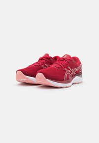 Pár červených a růžových běžeckých bot Asics s bílou podrážkou, umístěných vedle sebe na jednoduchém bílém pozadí.