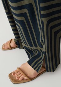 Wijd-uitlopende broek met groen en marineblauwe golvende strepen, gemaakt van zachte stof, gecombineerd met bruine platte sandalen met een enkelsteeks ontwerp.
