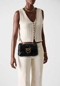 Zwarte gewatteerde handtas met een gouden ronde hardware accent en kettingband, crossbody gedragen. Heeft een gemêleerde stof en een uniek ontwerp.