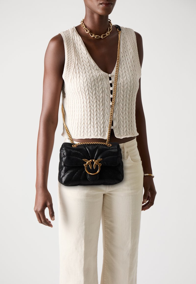 Zwarte gewatteerde handtas met een gouden ronde hardware accent en kettingband, crossbody gedragen. Heeft een gemêleerde stof en een uniek ontwerp.