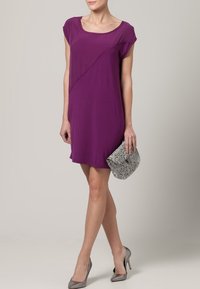 Lila kortärmad klänning med avslappnad passform, med diagonala sömdetaljer. Matchad med en silverfärgad clutch i ormskinn och grå klackar.