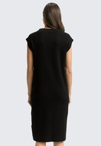 Zwarte, knielange jurk met kapmouwen, gladde textuur en een minimalistisch ontwerp. Achteraanzicht met een rechte silhouet en zonder versieringen.