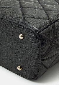 Sac matelassé noir avec un matériau texturé et un motif de logo embossé, agrémenté de ferrures couleur or sur le dessous.