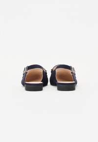 Zapatos sin espalda de ante azul marino con dos hebillas plateadas, tacones negros bajos y una plantilla de cuero suave. Diseño de suela plana.