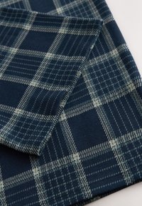 Gros plan d'un tissu bleu marine plié avec un motif à carreaux gris clair et des textures de lignes variées.