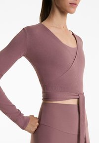 Duge rukave, top u stilu omote od mauve rebrastog materijala s prilagođenim dizajnom i detaljem vezanja na rubu, uparen s odgovarajućim donjim dijelom.