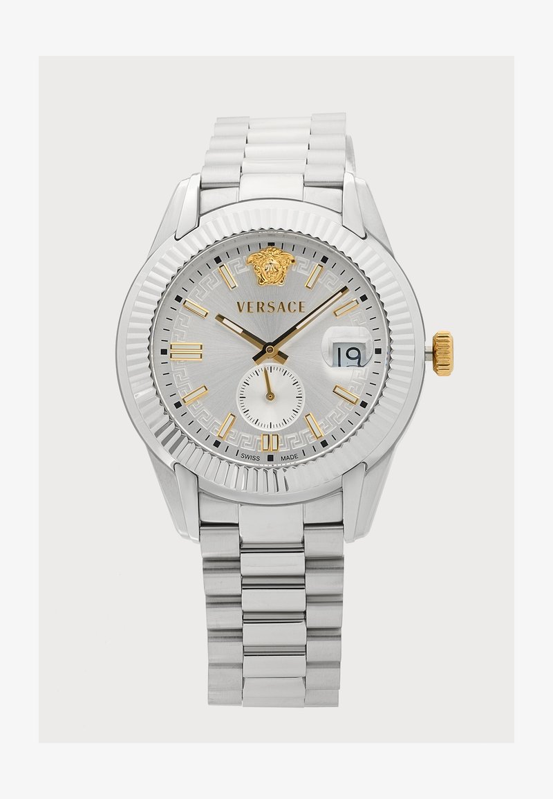Montre-bracelet Versace argentée avec des accents dorés, cadran blanc, fenêtre date affichant 19 et bracelet à maillons métalliques.
