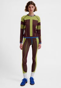 Stilfuldt træningstøj med en grøn og brun langærmet top med linjer og matchende tætsiddende leggings med kontrasterende sømme og detaljer.