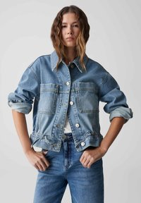 Lichtblauwe denimjas met een cropped ontwerp, twee voorzakken, zilveren knopen en een verstelbare taille. Heeft opgerolde mouwen.