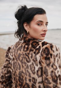 Puha tapintású leopárdmintás műszőrme kabát magas gallérral és ezüst színű fém díszítéssel a háton. A modell váll fölött néz hátra.