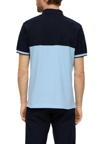 Granatowa i jasnoniebieska koszulka polo z blokowym wzorem kolorystycznym, krótki rękaw oraz biała lamówka przy kołnierzyku i rękawach, wykonana z bawełny.