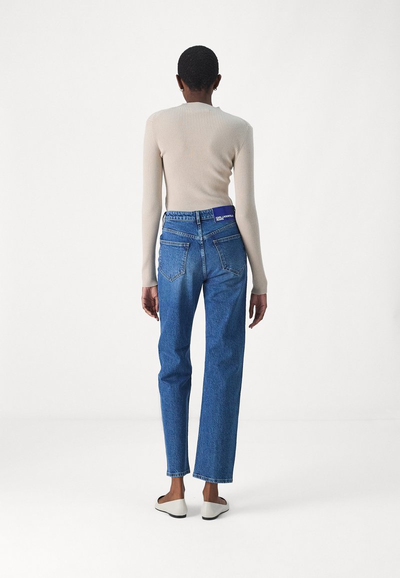 Blaue Jeans aus Denim mit geradem Schnitt, hoher Taille und Verblassen an den Oberschenkeln. Kombiniert mit einem beigen, gerippten Langarmoberteil.