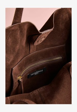 Brązowa torebka z zamszu o przestronnej wnętrzu, z kieszonką na zamek błyskawiczny, złotym zamkiem i logiem marki wewnątrz.