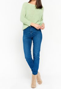 Pull en tricot vert clair avec une coupe ample, associé à un jean skinny bleu et des bottines beige. Texture lisse et design décontracté.