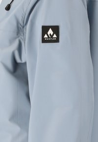 Helleblaue, wasserdichte Jacke mit glatter Textur, ausgestattet mit einem schwarzen Quadrat-Patch mit einem weißen Berglogo auf dem oberen Ärmel.