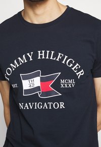 Navy blue cotton t-shirt featuring white and red printed graphics including a flag with "TH 42" and "NAVIGATOR," round neckline, short sleeves.