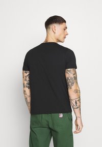T-shirt in cotone nero con scollo rotondo, maniche corte e vestibilità rilassata, abbinato a pantaloni verdi con dettaglio del taschino.
