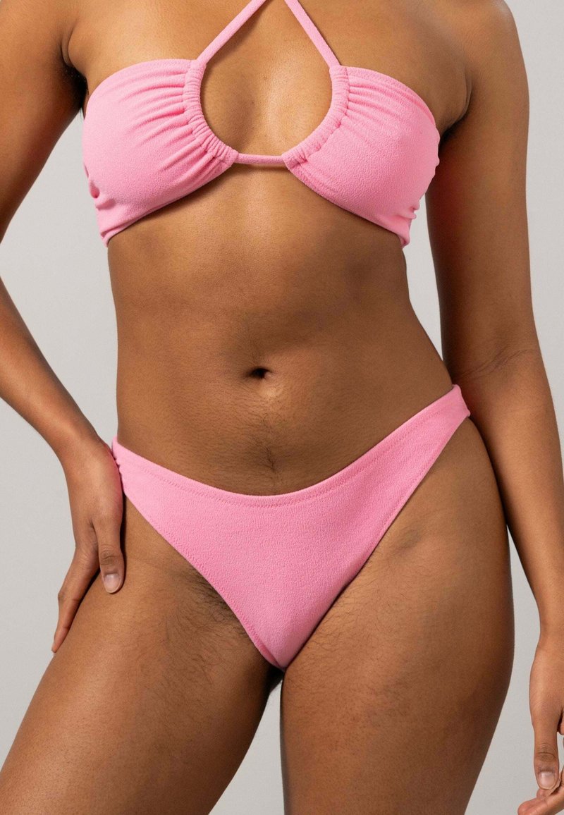 Rosa bikiniset med en strukturerad bandeau-overdel med veckdetaljer och ett lågt midjeband, båda i en enhetlig ljusrosa färg.