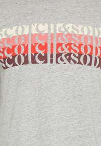 Grå bomulds t-shirt med et dristigt grafisk design med lagdelte bogstaver i creme, rød og mørk pink. Teksten lyder "SCOTCH & SODA."