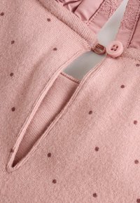 Rosa tröja med texturerat material, små bruna prickar, knappstängning och nyckelhålsöppning vid halsringningen.