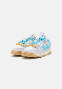 Sneakers a bassa altezza in pelle bianca e rete, con accenti turchesi, dettagli gialli e suola in gomma naturale. Lacci testurizzati e marchio.