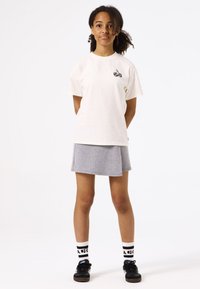 Camiseta de algodón blanca con un gráfico de cereza negra en el pecho, combinada con una falda gris con estampado y zapatillas negras con detalles blancos.