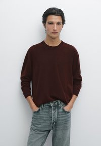 Maglione bordeaux a girocollo realizzato in tessuto morbido, abbinato a jeans in denim chiaro con vestibilità rilassata e delicate sfumature.