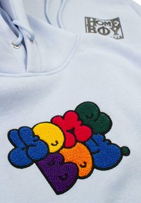 Hellblaue Kapuze mit einem bunten, strukturierten bestickten Design, auf dem das Wort "HOME BOY" in Rot, Gelb, Blau, Grün und Lila zu sehen ist.