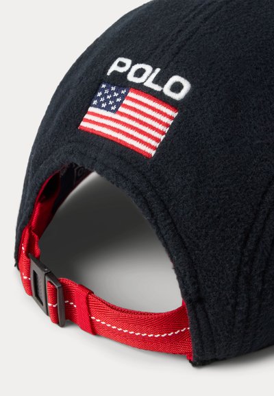 Schwarze Fleece-Mütze mit eingesticktem "POLO" und einer kleinen amerikanischen Flagge. Verfügt über einen roten, verstellbaren Riemen mit weißen Nähten auf der Rückseite.