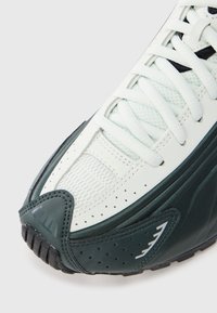 Vit och mörkgrön sneaker med texturerad ovansida, meshpanel, perforerade detaljer, platta skosnören och en gummisula med mönstrade slitbanor.