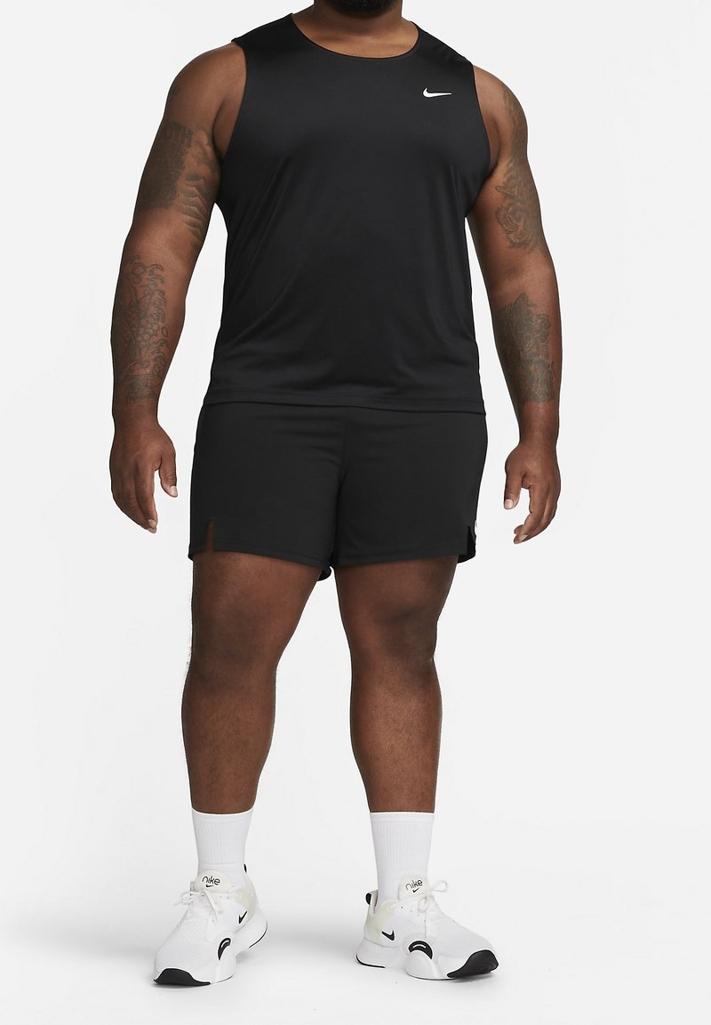 Haut de sport noir sans manches avec un col rond, associé à un short noir. Logo Nike blanc. Porté avec des baskets et des chaussettes blanches.