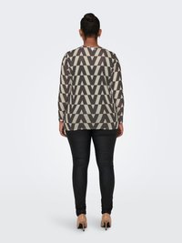 Long-sleeve top in geometric gray and cream pattern, paired with black fitted pants and beige heels. The top has a round neckline and relaxed fit.