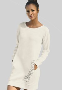 Weißes Langarmkleid aus weichem Stoff, mit lockerem Schnitt, rundem Ausschnitt und seitlichen Taschen, mit dem "Bench"-Logo nahe dem Saum bedruckt.