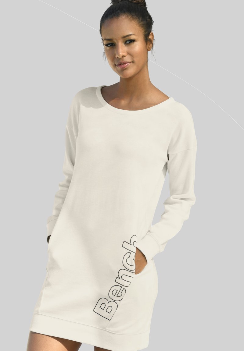 Weißes Langarmkleid aus weichem Stoff, mit lockerem Schnitt, rundem Ausschnitt und seitlichen Taschen, mit dem "Bench"-Logo nahe dem Saum bedruckt.