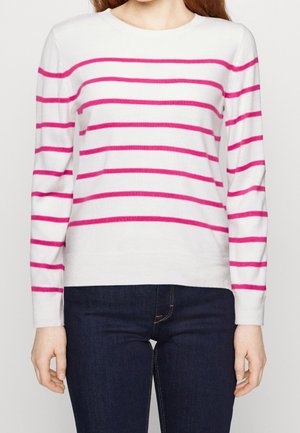 Maglione bianco a maniche lunghe con audaci strisce rosa. Colletto e polsini a coste. Abbinato a jeans blu scuro, che mostrano un look casual.
