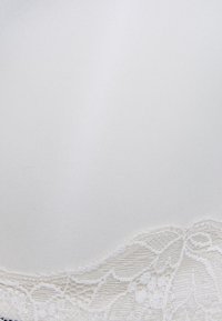 Bela satenasta modrca z občutljivim čipkastim robom na dnu. Gladka tekstura in brezšivna zasnova, ki prikazuje zapletene cvetlične vzorce v čipki.